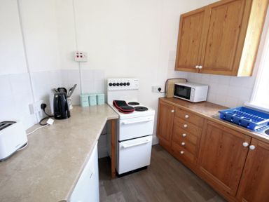 A kitchen with wooden cabinets a white stove a microwave a kettle toaster and a dish drying rack at Gullsway Sandpiper Polzeath