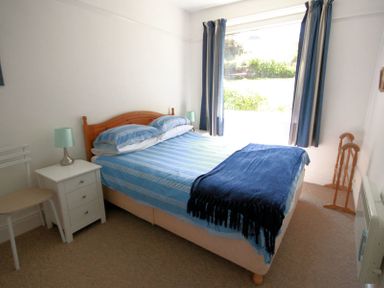 A bedroom with a bed desk chair and window with curtains at Gullsway Sandpiper Polzeath