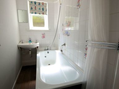 A bathroom with a bathtub a sink a window with a roller blind and a shower curtain at Gullsway Sandpiper in Polzeath