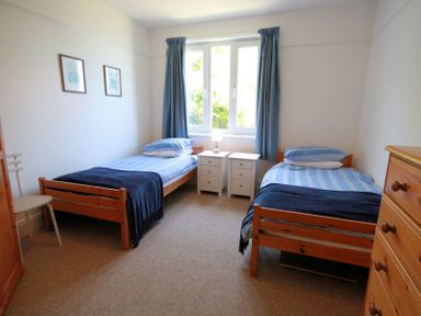A bedroom with two single beds bedside tables and a chest of drawers at Gullsway Sandpiper in Polzeath