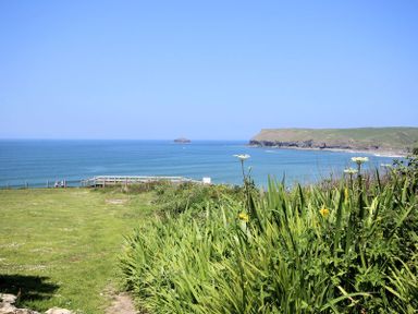 A coastal view with green grass and plants overlooking the sea with a rocky headland in the distance at Gullsway Sandpiper in Polzeath