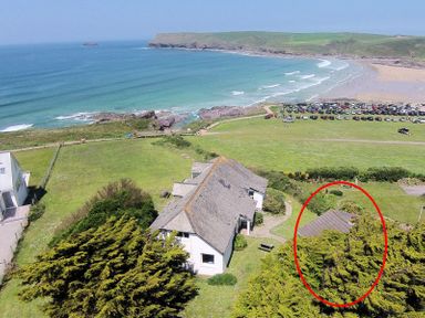 A coastal house with a grey roof near a beach with parked cars and waves at Gullsway September Tide in Polzeath