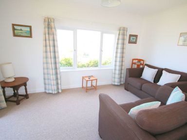 A living room with brown sofas white cushions a small wooden table lamp and plaid curtains at Gullsway September Tide in Polzeath