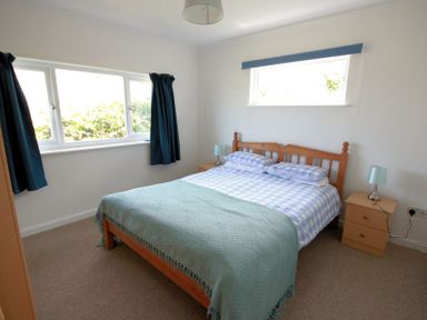 A bedroom with a wooden double bed two bedside tables and blue curtains at Gullsway September Tide in Polzeath