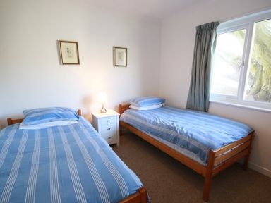 A bedroom with two single beds with blue striped bedding and a white bedside table with a lamp at Gullsway September Tide in Polzeath