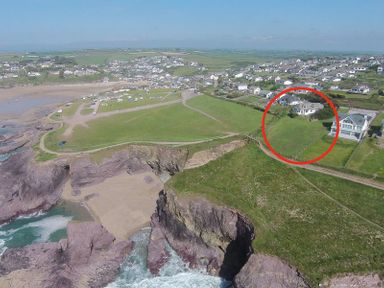 An aerial view of a coastal area with cliffs a beach houses and fields in Polzeath