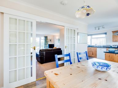 A kitchen and dining area with wooden furniture blue chairs and a living room with a brown sofa at Little Sailing in Rock