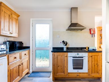 A kitchen with wooden cabinets appliances black countertop and a frosted glass door at Little Sailing in Rock