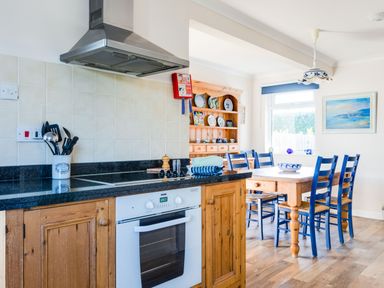 A kitchen with wooden cabinets black countertops a white oven blue chairs and a wooden dining table at Little Sailing in Rock