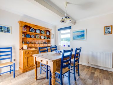A dining room with a wooden table and blue chairs a wooden dresser with plates on display and a window with a view at Little Sailing in Rock