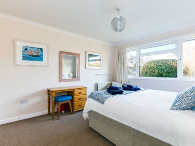 A bedroom with a bed, wooden desk with a blue stool, wall mirror, framed pictures, and a large window at Little Sailing in Rock
