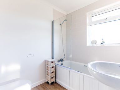 A bathroom with a bathtub and shower, a small wicker drawer unit, a sink, and a window at Little Sailing in Rock