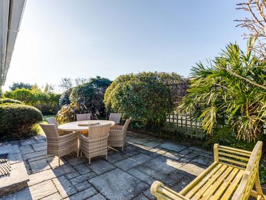 An outdoor patio with a round table and six chairs surrounded by trimmed bushes and a wooden bench at Little Sailing in Rock