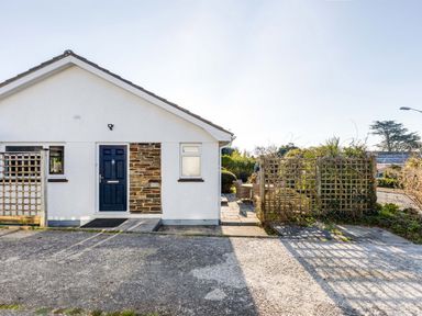 The exterior of a single-story house with a blue door stone wall section and adjacent patio area with chairs at Little Sailing in Rock