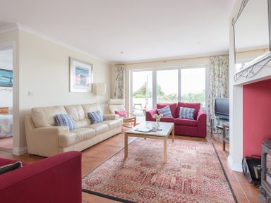 A living room with a cream sofa two red armchairs a coffee table and a television at Kirra in Polzeath