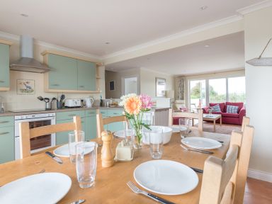 A dining table with plates glasses and flowers in a kitchen and living room at Kirra in Polzeath