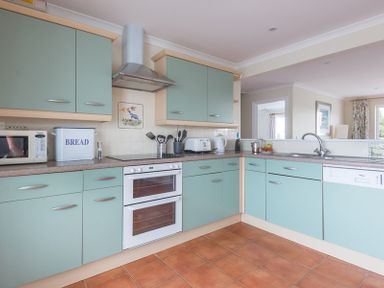 A kitchen with green cabinets a double oven a microwave a bread box and a dishwasher at Kirra in Polzeath