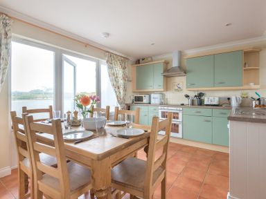 A kitchen with green cabinets wooden dining table with six chairs and flowers on the table at Kirra in Polzeath