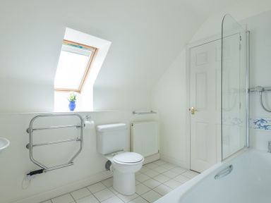 A bathroom with a toilet a bathtub with glass screen a skylight window and a radiator at Kirra in Polzeath