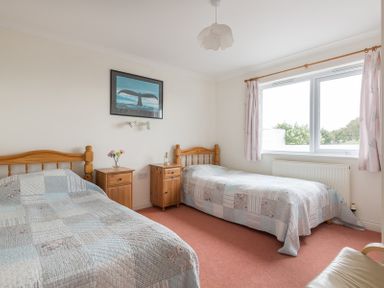 A bedroom with two single wooden beds two wooden bedside tables a painting on the wall and a window with curtains at Kirra in Polzeath
