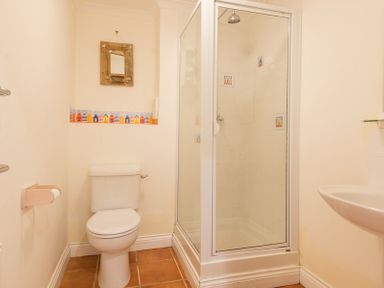 A bathroom with a toilet a shower cubicle a wall-mounted sink and a mirror at Kirra in Polzeath