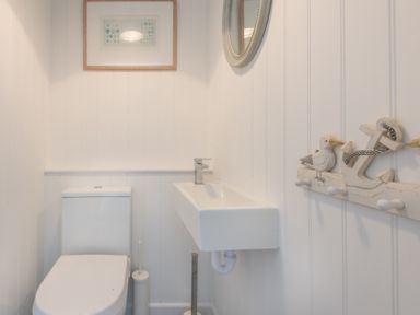 A small bathroom with a toilet and a wall-mounted sink with a faucet and nautical-themed hooks on the wall at Porthilly Brook in Rock