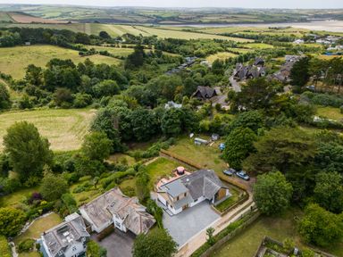 Aerial view of houses surrounded by trees fields and a river in the distance at Porthilly Brook Rock