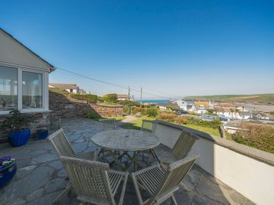 A stone patio with a round wooden table and six chairs overlooking houses and the sea at Pentire View (3) in Polzeath