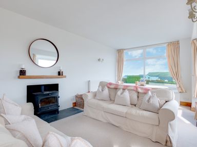 A living room with two sofas a wood stove and a large window with curtains at Pentire View Polzeath