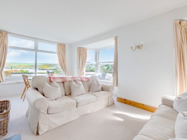 A living room with two sofas cushions and large windows showing a grassy landscape at Pentire View (3) in Polzeath