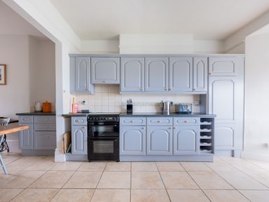 A kitchen with grey cabinets black oven kettle toaster and tile floor at Pentire View (3) in Polzeath