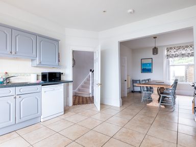 A kitchen with gray cabinets a dishwasher a microwave and a dining area with a wooden table and gray chairs at Pentire View in Polzeath