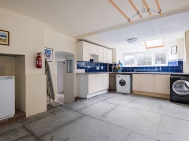 A utility room with washing machines cabinets a skylight and an ironing board at Pentire View (3) in Polzeath