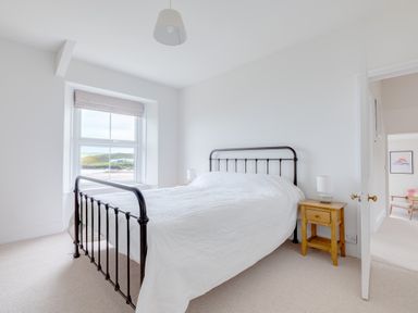 A bedroom with a metal bed frame wooden bedside table and a window showing an outdoor view at Pentire View (3) in Polzeath