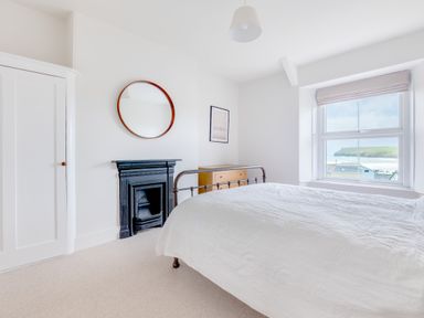 A bedroom with a bed and a wooden chest of drawers near a window showing an outside view at Pentire View (3) in Polzeath