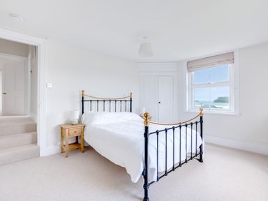 A bedroom with a metal bed frame wooden bedside tables and a window showing a sea view at Pentire View (3) Polzeath