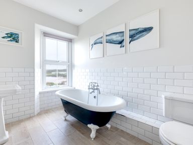 A bathroom with a clawfoot bathtub under a window and whale art on the wall at Pentire View (3) in Polzeath