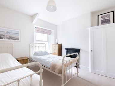 A bedroom with two single metal beds a wooden nightstand a chest of drawers a black fireplace and a white wardrobe at Pentire View in Polzeath