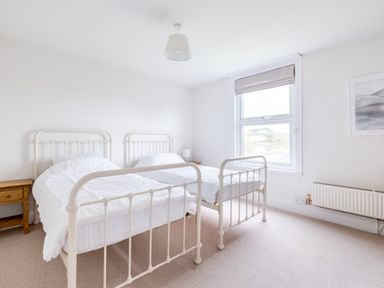 A bedroom with two single metal beds a bedside table a window and radiator at Pentire View (3) in Polzeath