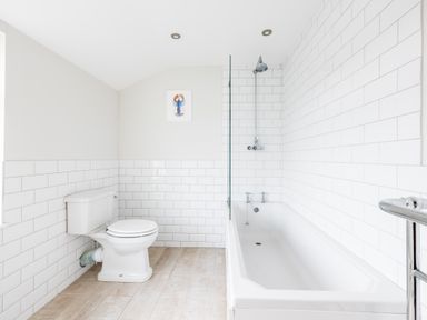 A bathroom with a toilet bathtub showerhead and tiled walls at Pentire View in Polzeath