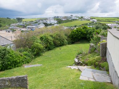 A grassy garden area with stone steps and shrubs overlooking a village and green fields at Pentire View (3) in Polzeath