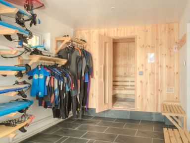 A room with surfboards on racks wetsuits hanging and a wooden sauna at Treverden in Polzeath