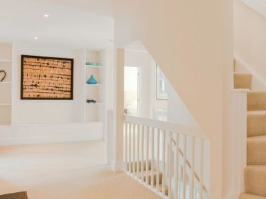 A hallway with beige carpet stairs white railing built-in shelves with blue decor and a framed artwork at Treverden Polzeath
