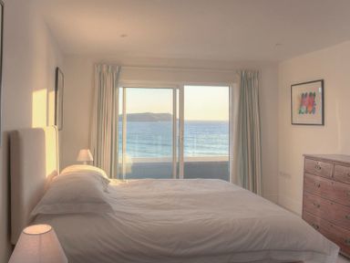 A bedroom with a bed facing glass sliding doors showing an ocean view at Treverden in Polzeath