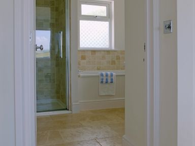 A bathroom with a glass shower enclosure bathtub with towels and a window at Treverden Polzeath
