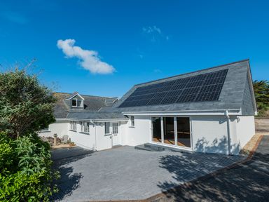 A white house with solar panels on the roof and a paved driveway at Treverden in Polzeath
