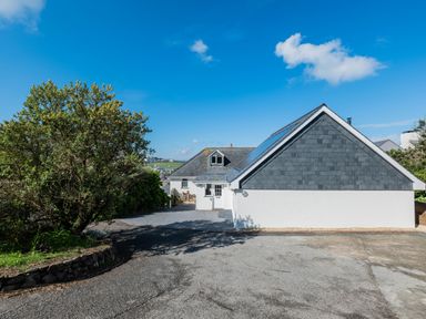 A driveway with a white house and a tree under a blue sky at Treverden Polzeath