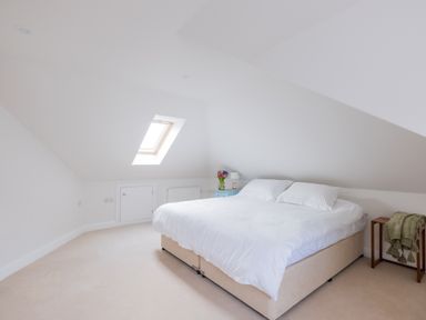 A bedroom with a bed side table flowers lamp and a skylight window at Treverden in Polzeath