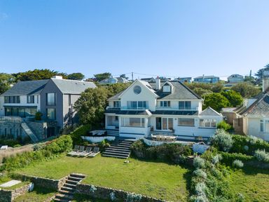 A large house with multiple windows a patio with outdoor furniture and lawn chairs on a green lawn at Treverden in Polzeath