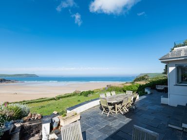A patio with dining table and chairs overlooking a beach and ocean at Treverden in Polzeath